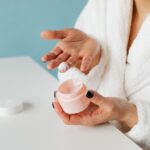A person in a white bathrobe applies scar care gel from an open jar onto their hand, representing the topical gel format covered by Malaysia's OEM scar care manufacturers in this 2026 list.