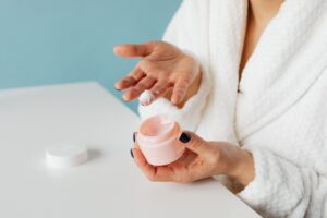 A person in a white bathrobe applies scar care gel from an open jar onto their hand, representing the topical gel format covered by Malaysia's OEM scar care manufacturers in this 2026 list.