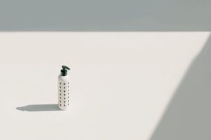 Minimalist white pump bottle with a green cross pattern on a plain background, representing the gentle, dermatologically-tested formulations typical of baby and sensitive-skin care contract manufacturing.