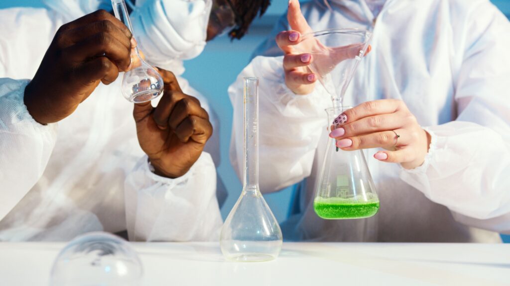 Two lab technicians in white coats handling glass flasks with a green liquid sample during a quality check, representing the certification and quality-control verification buyers should confirm before choosing a Malaysia-based OEM personal or medical lubricant manufacturer.