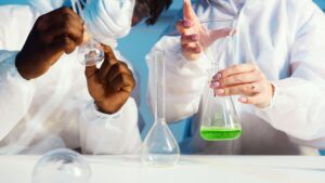 Two lab technicians in white coats handling glass flasks with a green liquid sample during a quality check, representing the certification and quality-control verification buyers should confirm before choosing a Malaysia-based OEM personal or medical lubricant manufacturer.